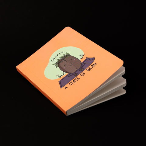 An orange notebook with an image of a coffee bean wearing a wreath and meditating 